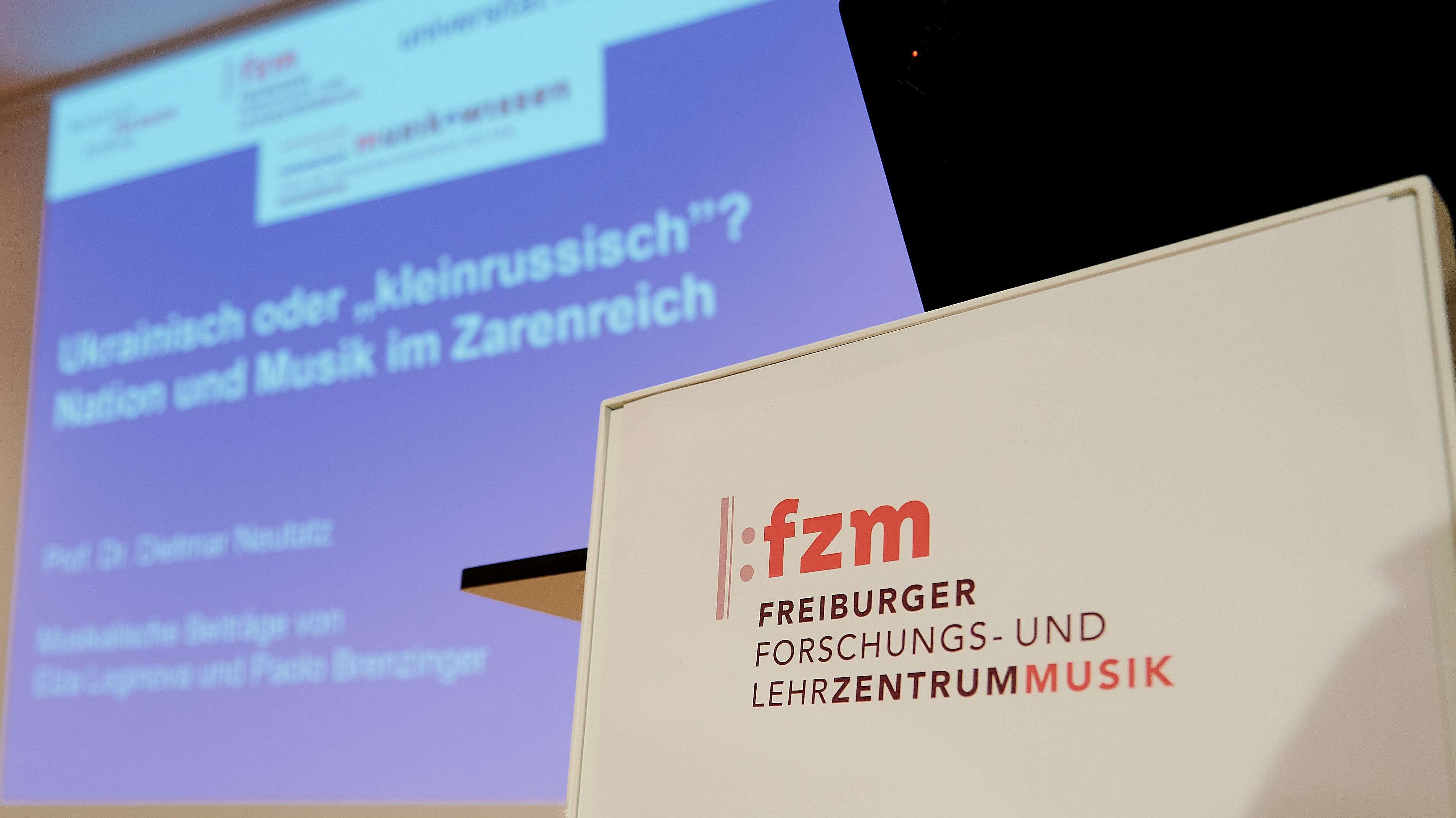 FZM Logo, im Hintergrund sieht man verschwommen eine Leinwand